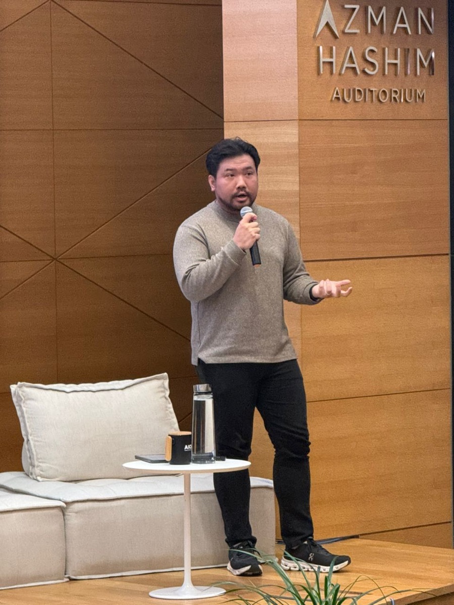 Isaac Tan speaking on stage at the Azman Hashim Auditorium, Kuala Lumpur.